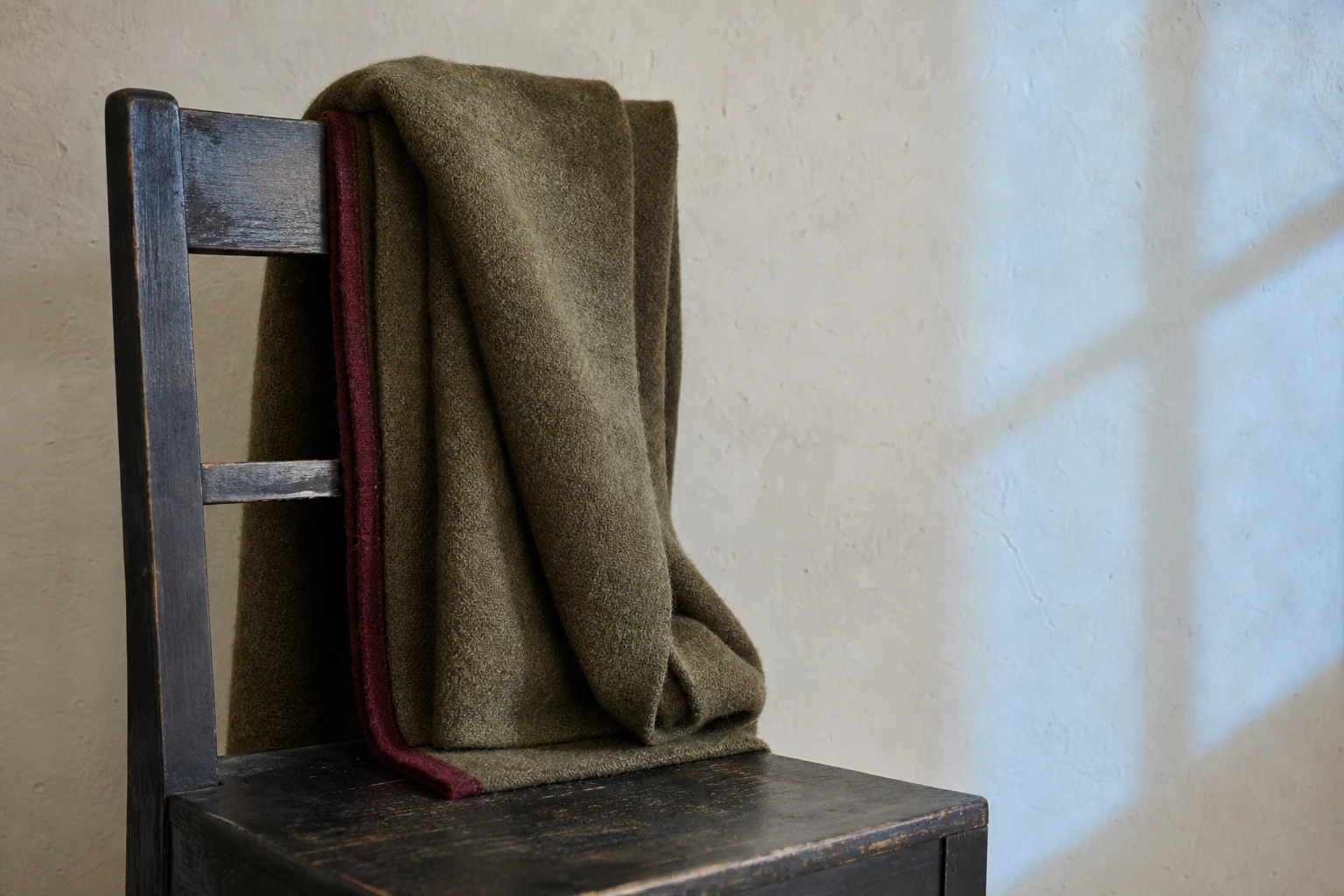 Couverture en laine olive posée sur une chaise en bois sombre
